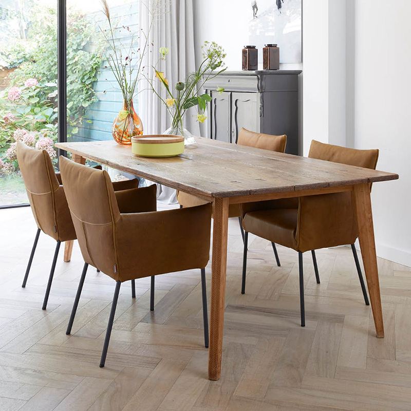 Eetkamer met houten tafel en bruine leren stoelen Mali van LABEL Vandenberg, ingericht met decoratieve vazen en een groene tuin op de achtergrond